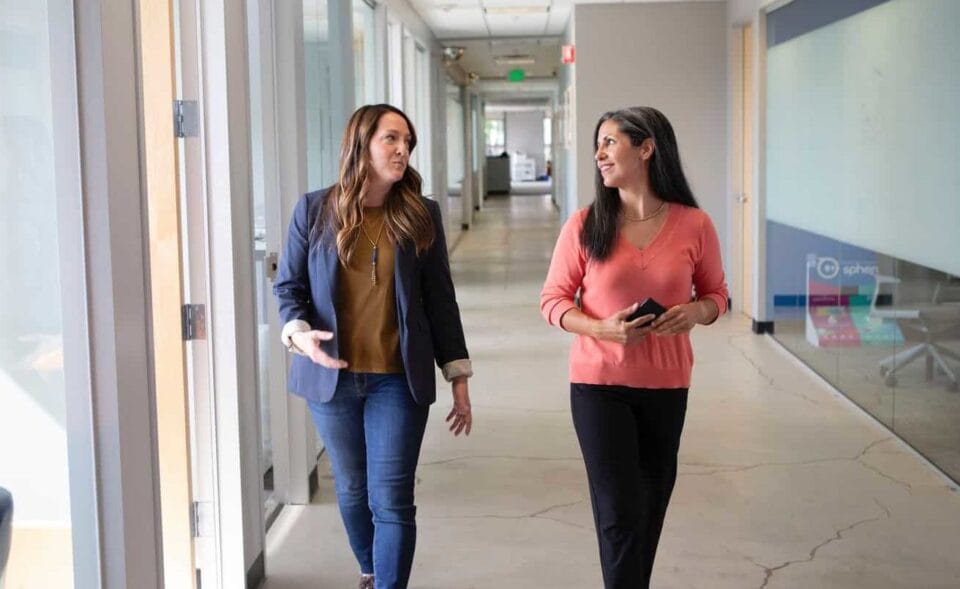Kaksi naista kävelemässä ja keskustelemassa toimistolla. Johtajasopimus on tärkeä osa ylemmän johdon työturvaa.